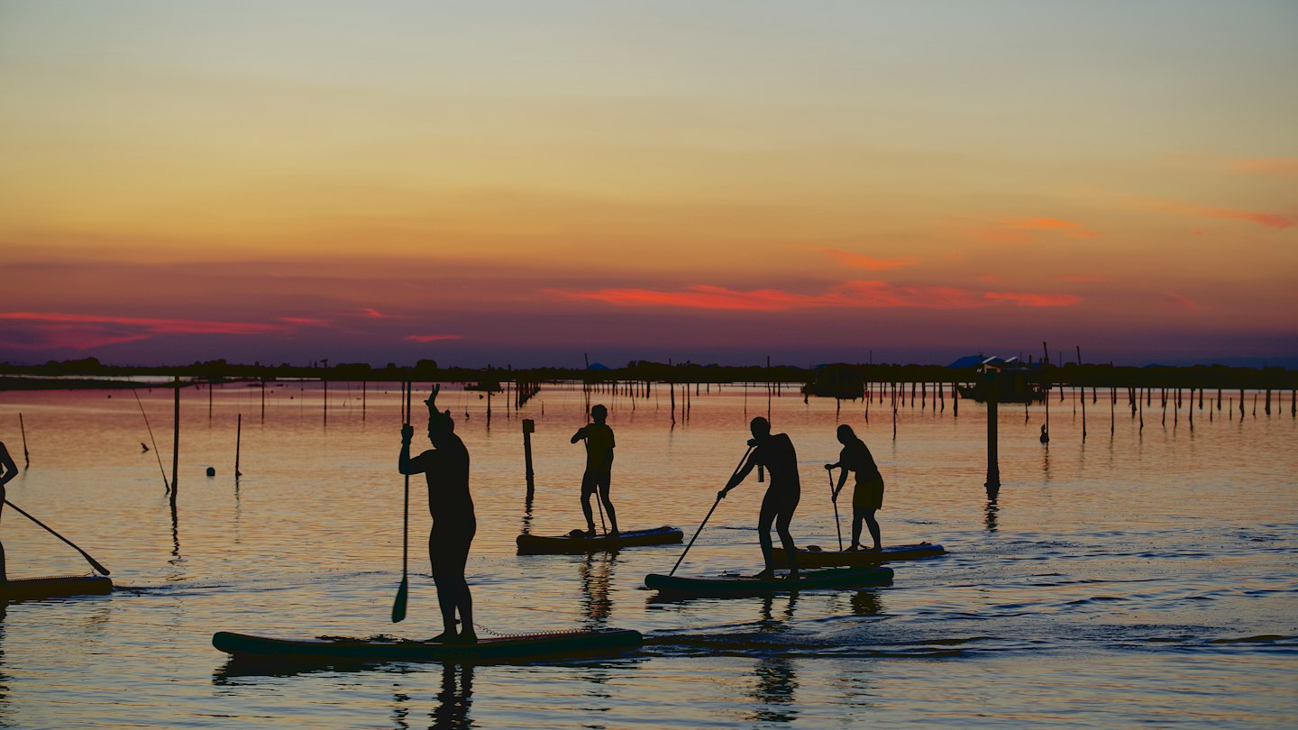 Persone fanno paddleboard sull'acqua vicino a una costa lontana.